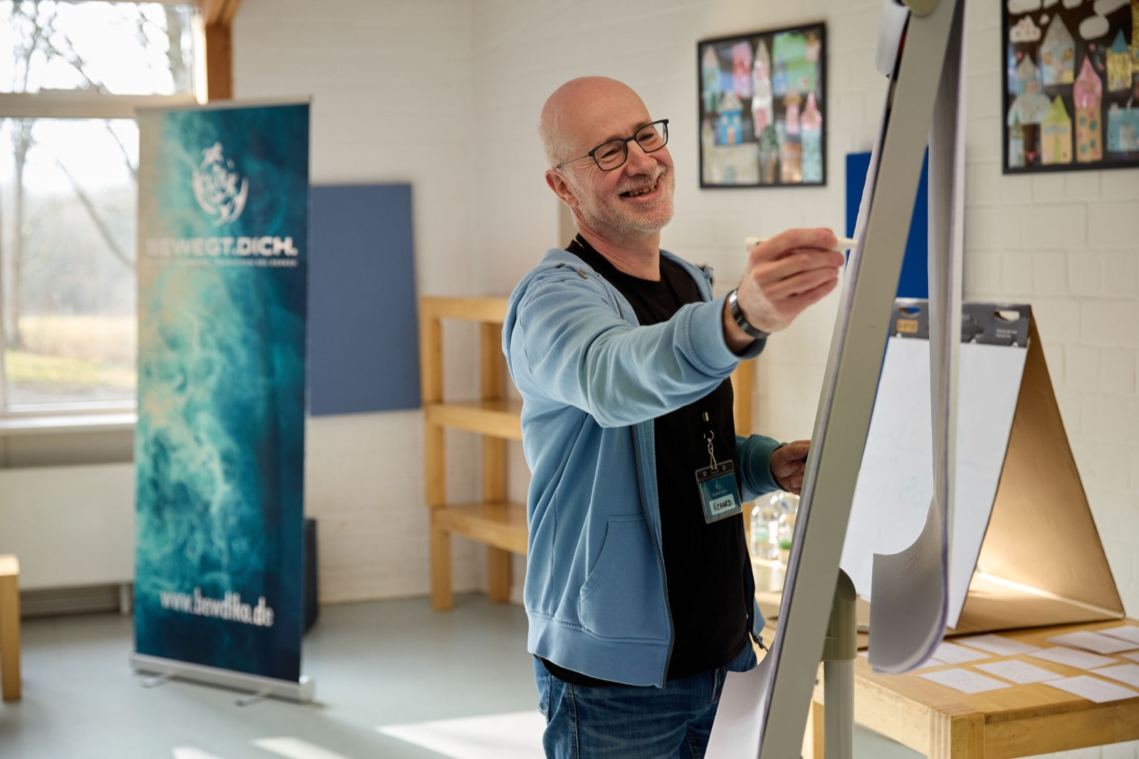 Referent Richard Beck schreibt lachend am Flipchart, im Hintergrund ein BEWEGT.DICH®-Banner